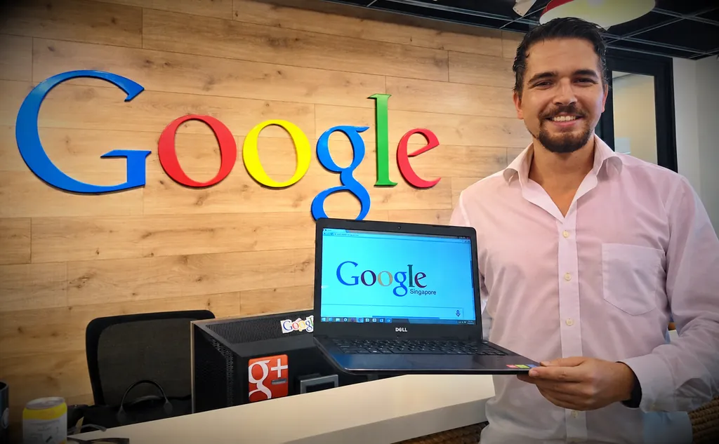 Frederik Neust zu Gast bei Google in Singapur, mit Laptop vor dem Google-Logo an einer Holzwand