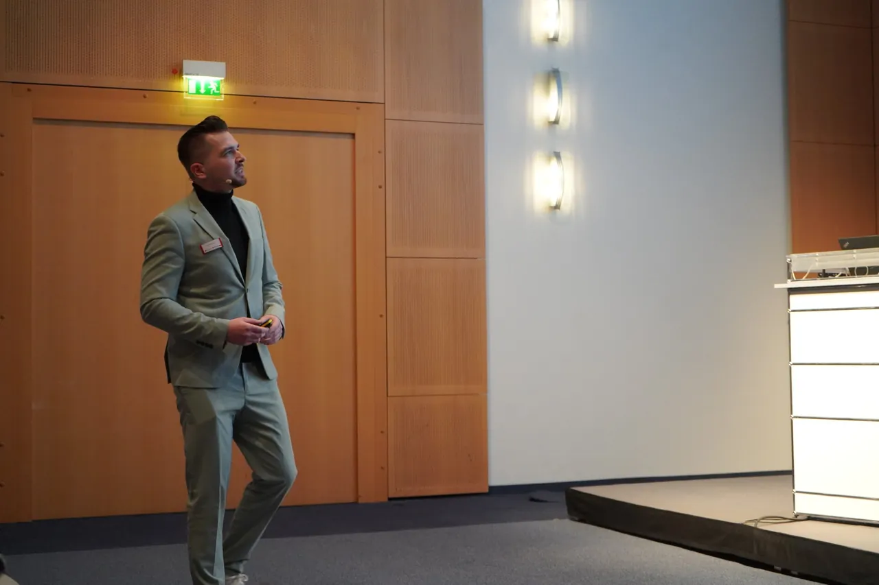 Frederik Neust im hellgrünen Anzug blickt während seines Vortrags beim FIBO Congress 2024 zur Leinwand