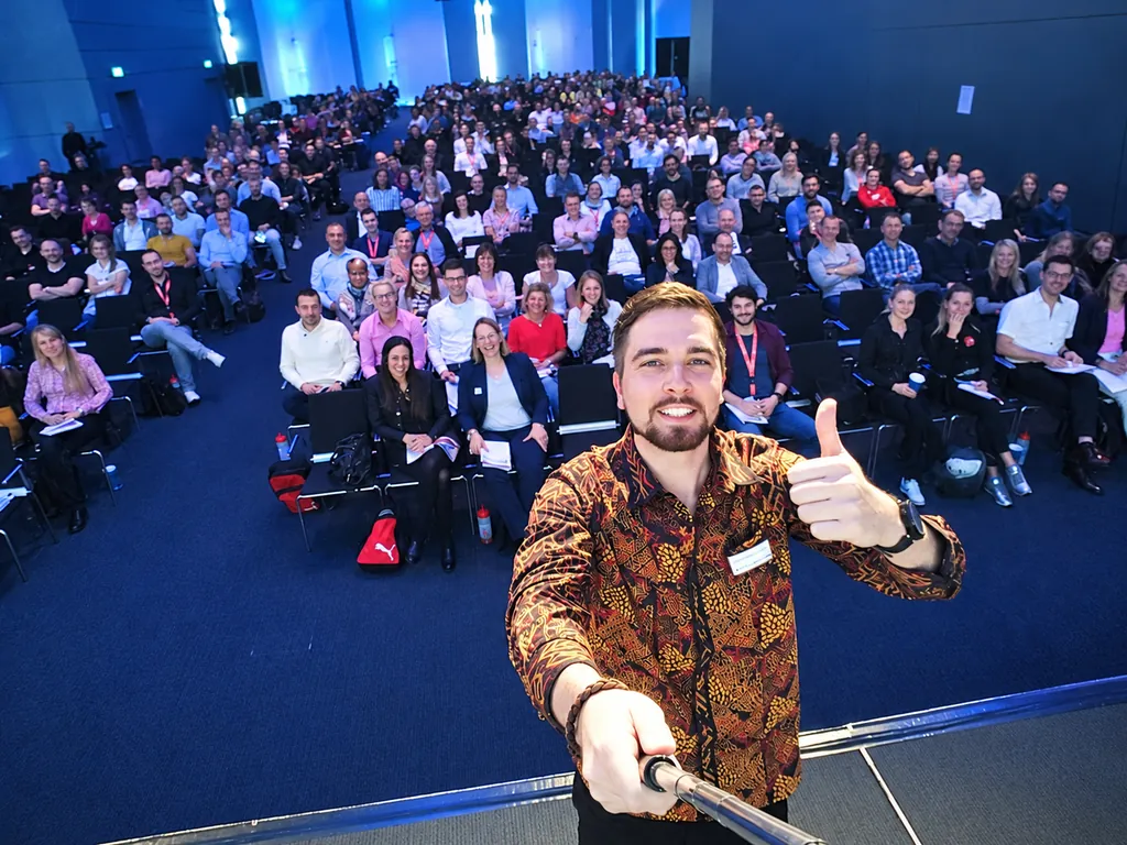 SEO-Speaker Frederik Neust macht beim Aufstiegskongress 2017 ein Selfie mit erhobenem Daumen, hinter ihm das voll besetzte Publikum